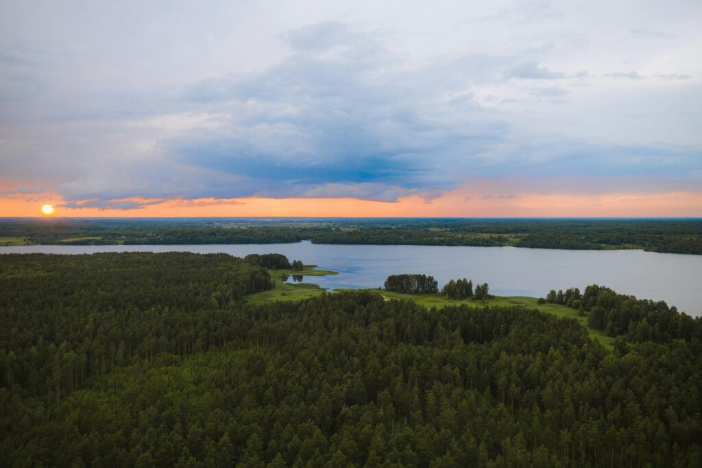 Aerial view of a scenic sunset over a tranquil lake and dense forest in Tver Oblast, Russia.
