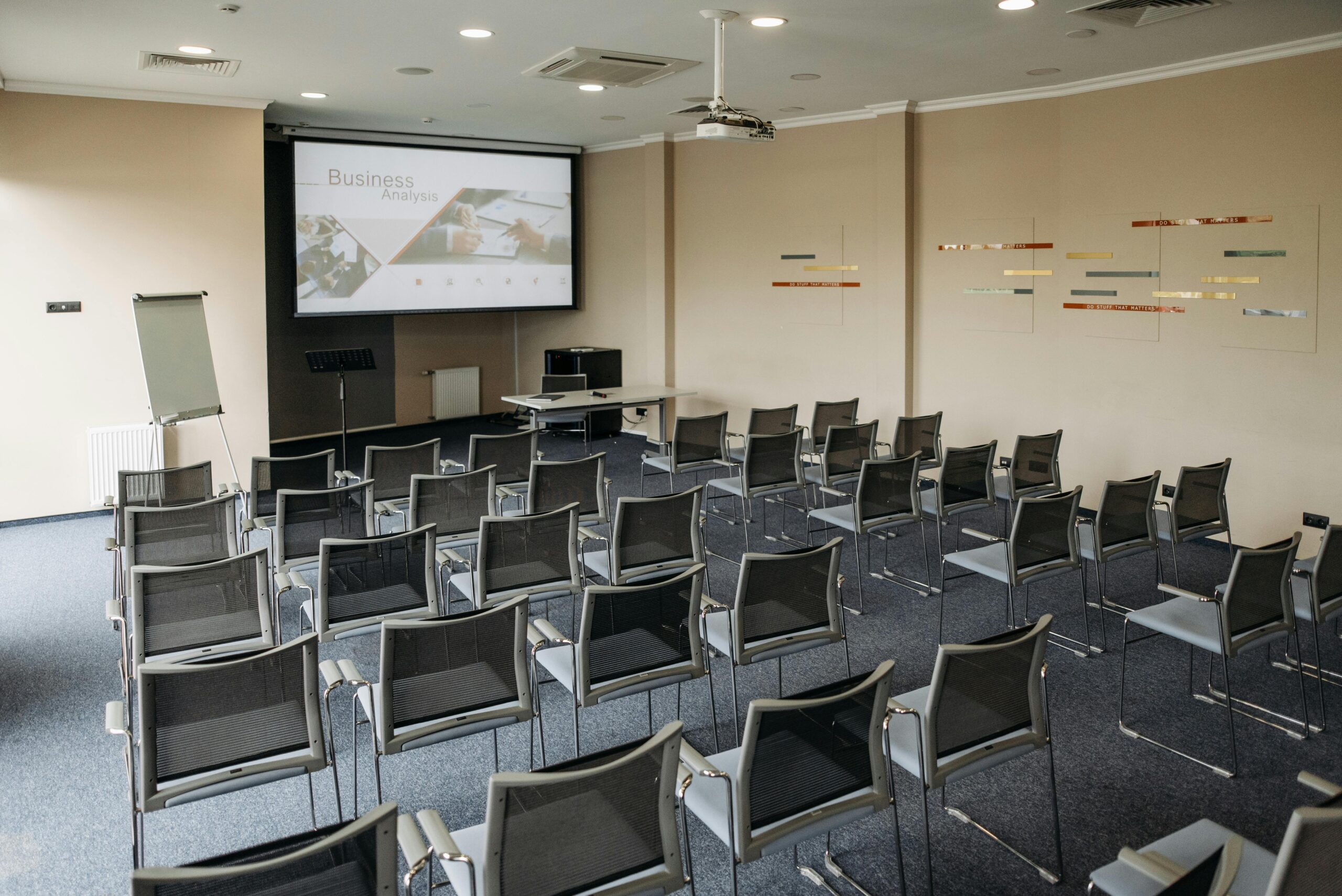 Empty conference room featuring rows of chairs, screen, and whiteboard.